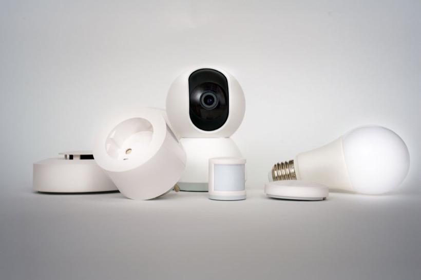A small Wi-Fi camera next to a smoke-detector-style sensor and a smart bulb, the kind of everyday devices a hidden lens can hide inside