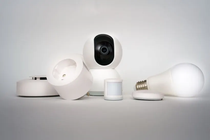 A small Wi-Fi camera beside a smoke-detector-style sensor and a smart bulb, the kind of devices a hidden lens can hide inside
