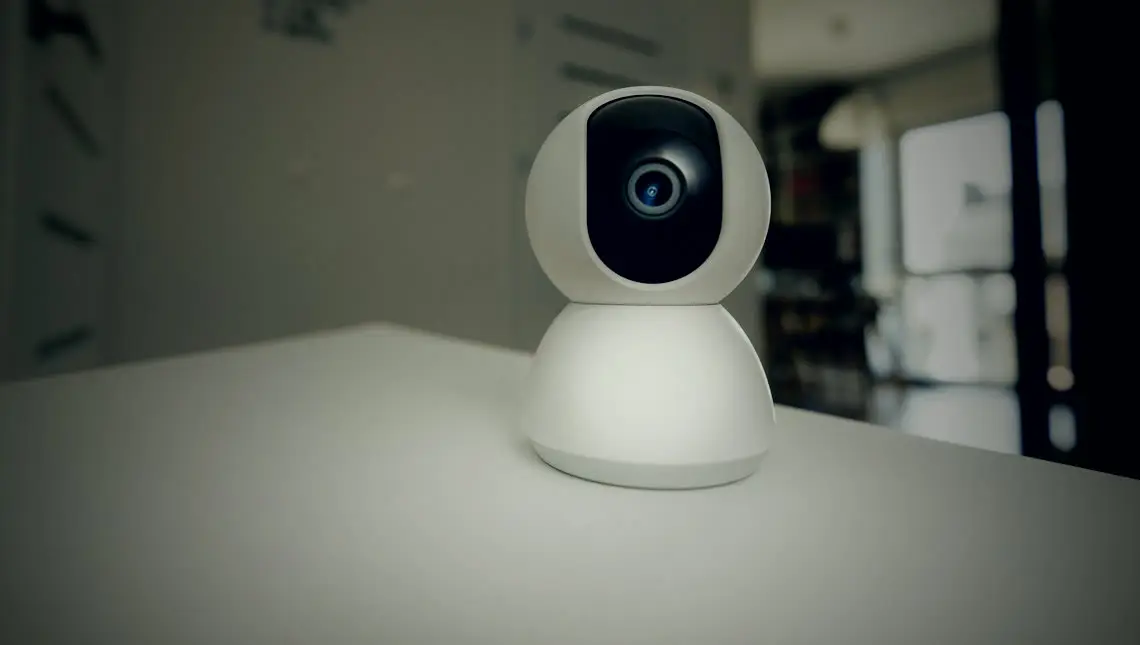 A small indoor security camera on a table, lens pointed into the room